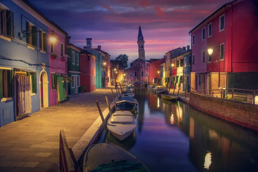 Colourful houses and boats along a canal in Burano, Venice, at dusk