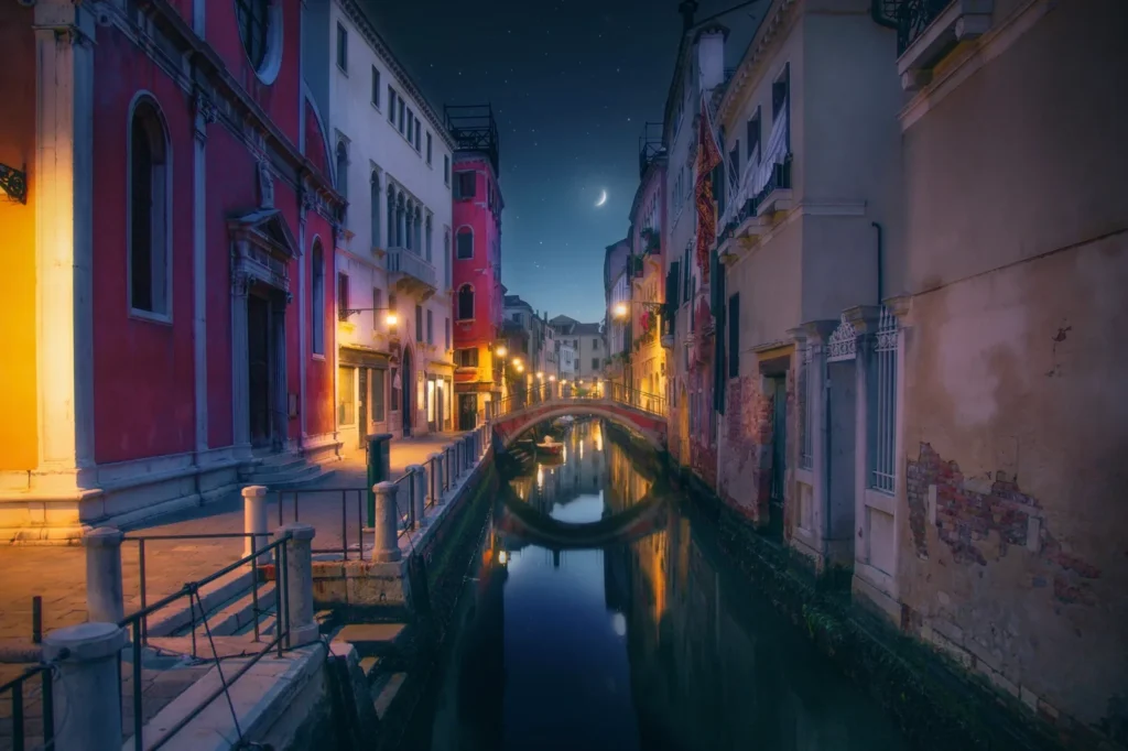 A quiet Venice canal at night under a crescent moon